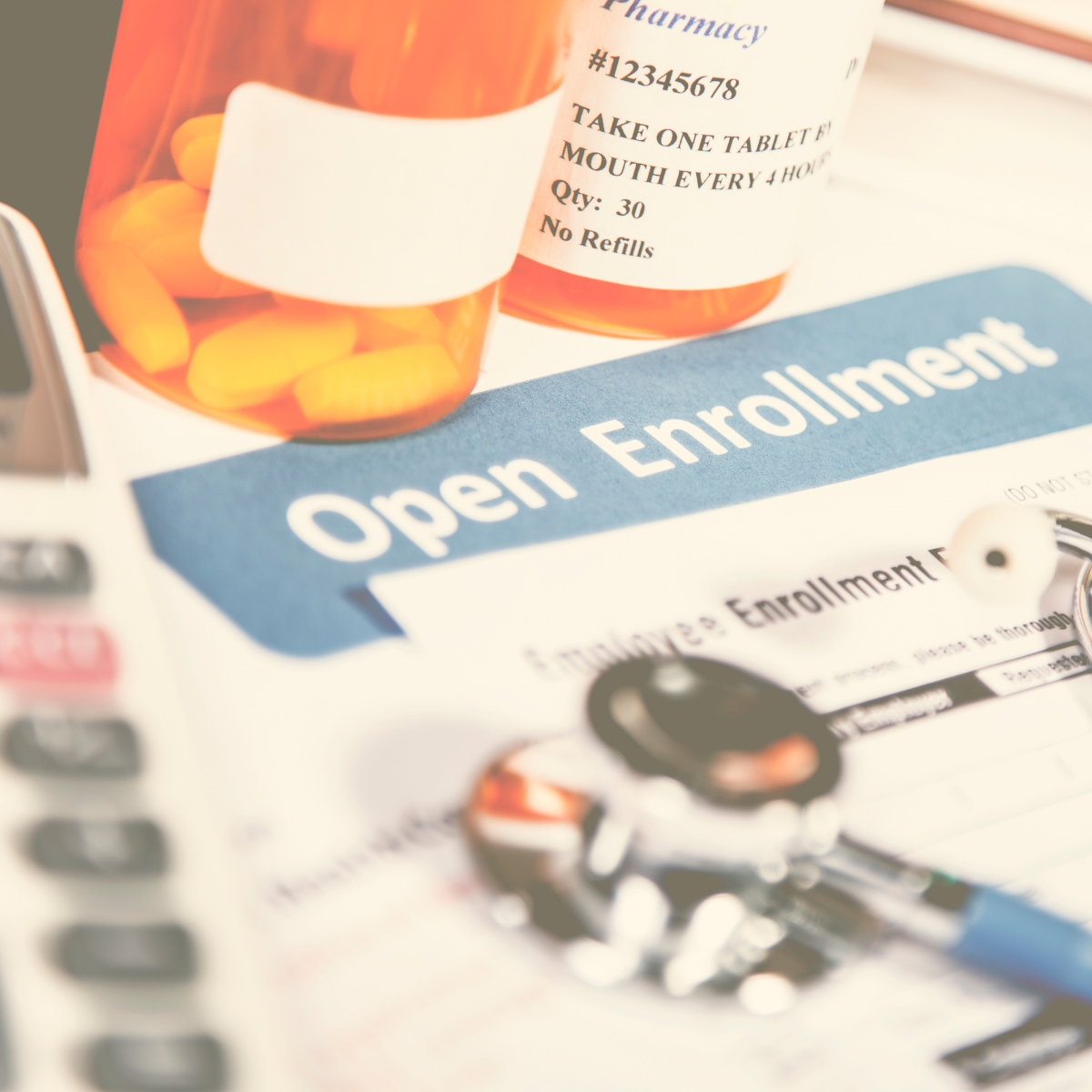 Open enrollment booklet laying on a table with a calculator, prescription bottles, and a stethoscope
